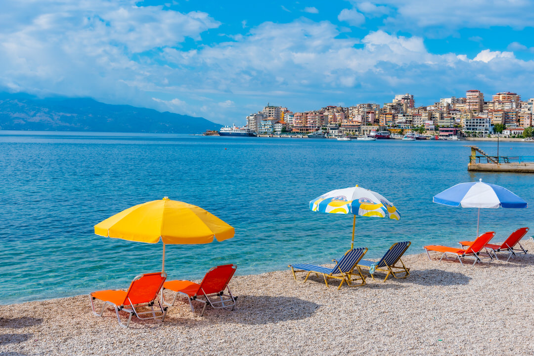 Parasols and loungers on the shingle at Saranda, the town waterfront across the bay