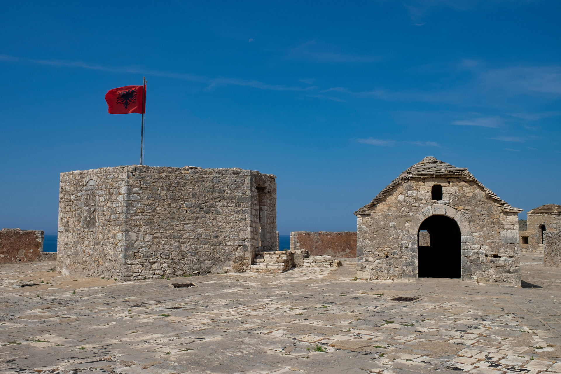 The Albanian flag over the stone keep of Porto Palermo castle, the Ionian beyond it